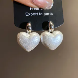 Close-up of elegant retro silver needle heart earrings with shimmering pearl texture