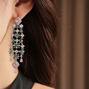 Close-up of elegant flower tassel earrings with pink and green stones on a model.