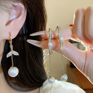 Close-up of elegant 18K gold plated fish tail and ribbon pearl earrings worn on ear