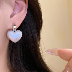 Pearlescent heart drop earrings with silver stud shown worn on ear for detail.