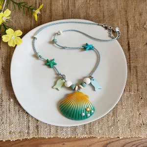 Close-up of ceramic shell pendant necklace with starfish and fish charms on white plate
