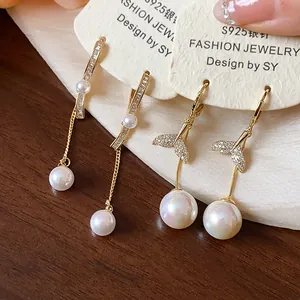 Macro view of 18K gold-plated mermaid tail and drop pearl earrings with CZ details.