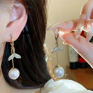 Close-up of 18K gold-plated zircon fish tail earrings with large pearl drop detail.