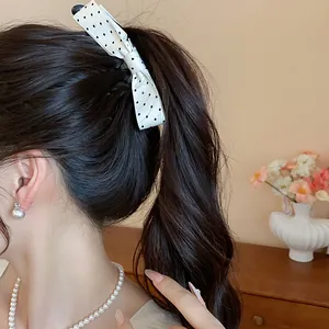 Detail view of an elegant white polka dot fabric bow hair clip styled in a high ponytail