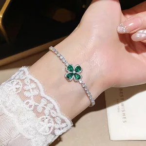Close-up of a sparkling silver bracelet with a green zircon clover charm on a wrist.