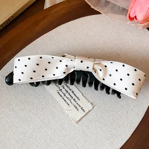 Elegant white fabric bow hair clip with black polka dots shown in a lifestyle detail view