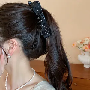 Detail shot of a black polka dot fabric bow claw clip worn on a high ponytail