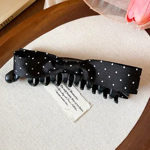 Detailed macro shot of a sweet black fabric bow banana hair clip with white polka dots