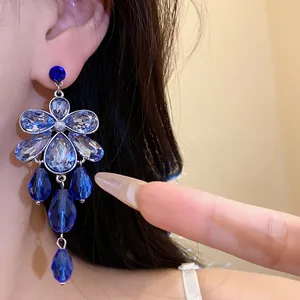 Close-up detail of elegant blue floral drop earrings with sparkling crystal accents.