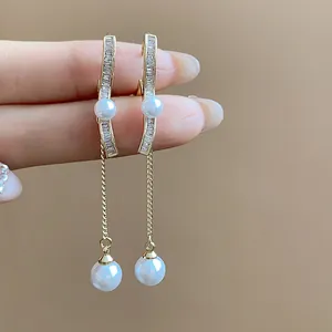 Macro detail of 18K gold-plated drop earrings featuring sparkling zircons and white pearls