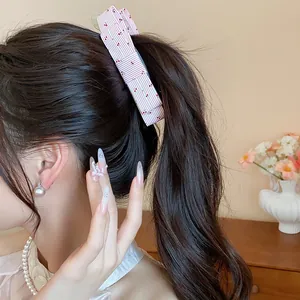Detail view of an elegant pink striped fabric bow twist hair clip on a high ponytail