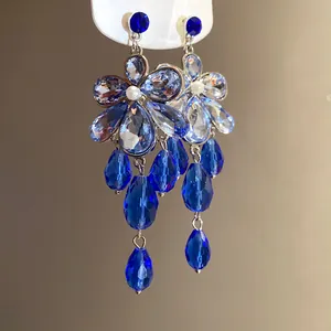 Macro detail of elegant silver-tone flower earrings with vibrant blue crystal teardrops