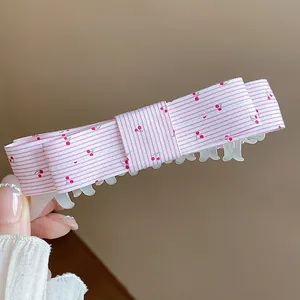Close-up of a sweet pink fabric bow hair clip with cherry patterns and stripe texture