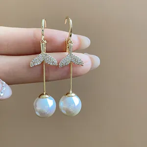 Close-up detail of 18K gold plated fish tail earrings featuring sparkling zircons and large pearls
