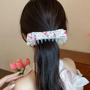 Detail view of a floral print fabric bow hair claw clip worn on long dark hair.