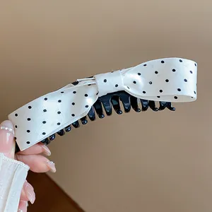 Macro view of sweet white polka dot fabric bow hair clip with black twist banana clip