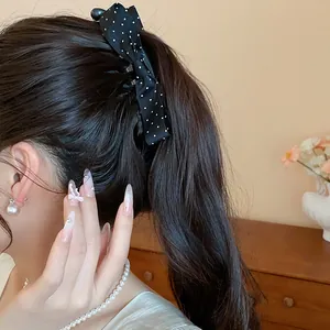Elegant black fabric polka dot bow hair clip styled on a brunette high ponytail.