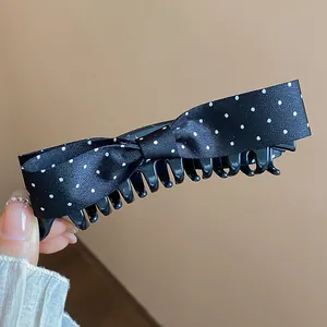 Detail shot of a black polka dot bow banana hair clip with elegant satin fabric