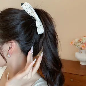 Close-up view of a white fabric bow hair clip with black polka dots on a wavy ponytail.