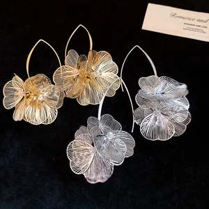 Detailansicht von hohlen Metallblumen-Ohrringen in Gold und Silber auf Schwarz.