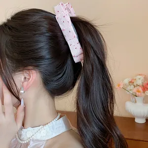 Detailed view of a pink striped bow hair clip with cherry pattern on a ponytail.