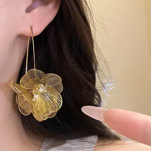 Nahaufnahme der eleganten goldenen, hohlen Metallblumen-Ohrhänger am Ohr eines Modells