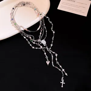 Dettaglio della collana a strati argento con ciondoli a croce e cuore su sfondo nero.