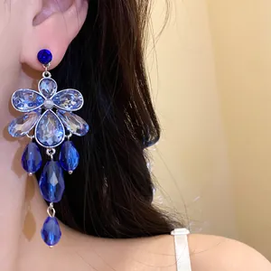 Detailed shot of elegant blue crystal flower earrings with teardrop pendants on model