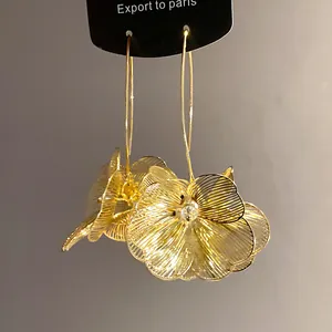 Nahaufnahme von goldenen Hohlblumen-Ohrringen mit filigranen Blütenblättern.