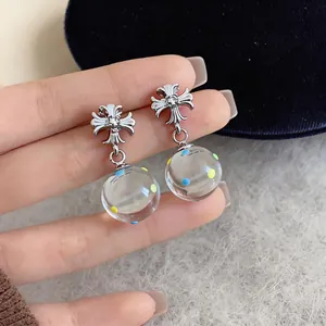 Close-up of silver cross drop earrings with colorful dotted glass balls for women