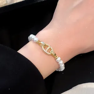 Nahaufnahme eines Perlenarmbands mit goldener, zirkonia-besetzter Ankerkettenschließe