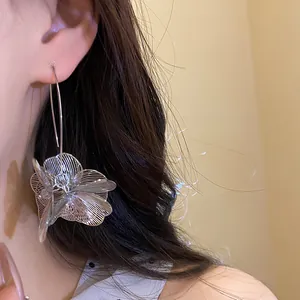 Detailaufnahme von eleganten, silbernen, hohlen Metallblumen-Ohrringen an einem Modell