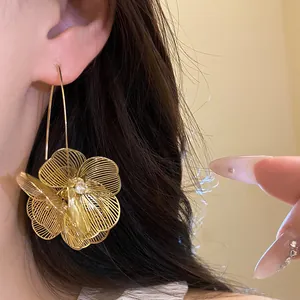 Elegante goldene hohle Blumenohrringe mit filigranen Details am Ohr fotografiert
