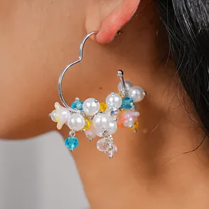 Close-up detail of heart-shaped hoop earrings featuring white faux pearls and blue crystals