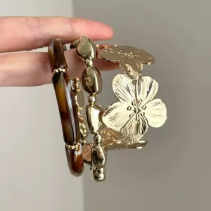 Close-up of elegant gold flower cuff and tortoiseshell resin bracelets held by hand.