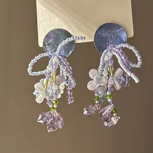 Vue détaillée de boucles d'oreilles en perles violettes avec gouttes de cristal.