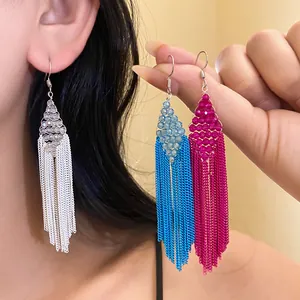 Main présentant des boucles d'oreilles bohèmes colorées à pompons avec des perles acryliques.