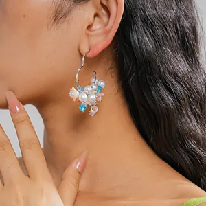 Detailed view of colorful faux pearl and blue crystal bead hoop earring on a model