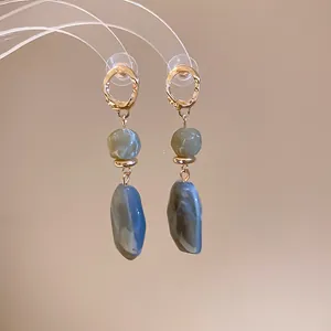 Close-up of resin irregular geometric drop earrings with marbled texture and gold ring.