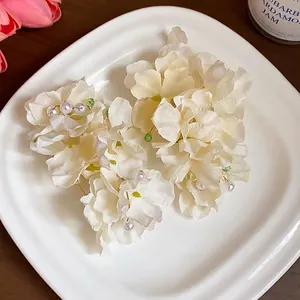 Elegant cream fabric flower hair clips with pearls and green beads displayed on a white plate
