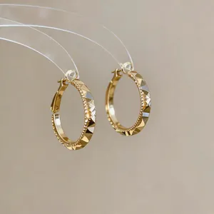 Close-up of faceted gold hoop earrings with beaded edge and geometric design.