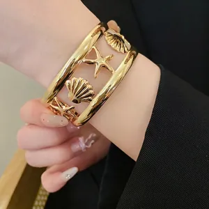 Elegant gold cuff bracelet with starfish and seashell cutout designs worn on model wrist