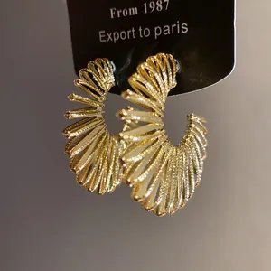 Macro view of gold textured spiral C-shaped hoop earrings with intricate metallic finish