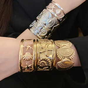 Close-up detail of gold and silver starfish and shell hollow cuff bracelets on wrist
