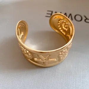 Close-up of gold starfish and shell relief on a matte textured open cuff bracelet.