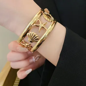 Close-up of a gold starfish and seashell hollow open cuff bracelet on wrist.
