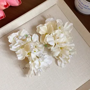 Detailed view of white fabric flower hair clips with pearls on a textured display board.