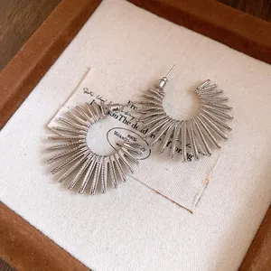 Detail view of silver-tone sunburst geometric C-shaped hoop earrings in a jewelry box.