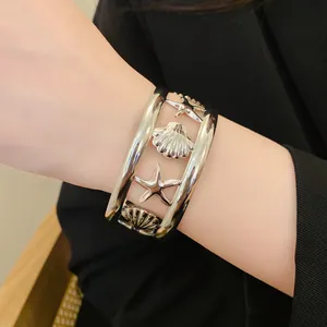 Macro detail of silver-toned hollow starfish and seashell open cuff bracelet on a wrist