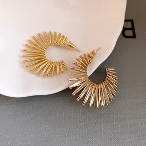 Detailed view of gold C-shaped earrings with unique sunburst texture and silver needles.